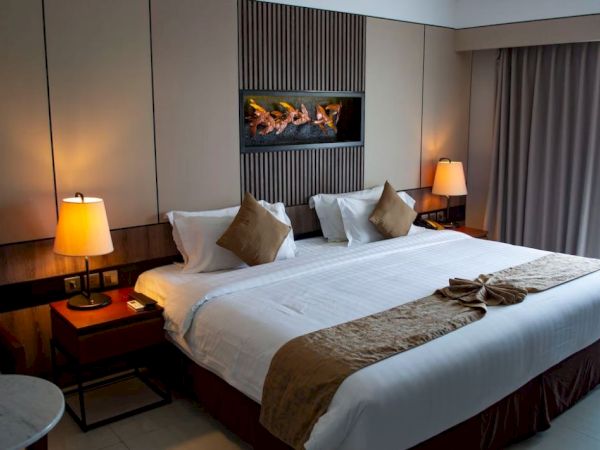 A cozy hotel room with a large bed, two bedside lamps, and a wall decoration, featuring warm lighting and elegant furnishings.