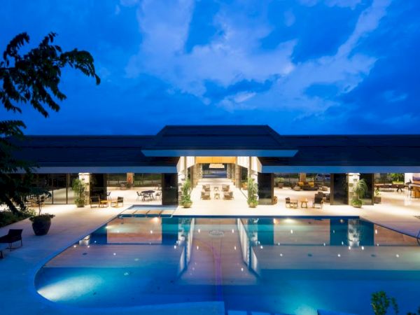 A luxurious modern building with an illuminated, spacious outdoor pool and seating area under a twilight sky.