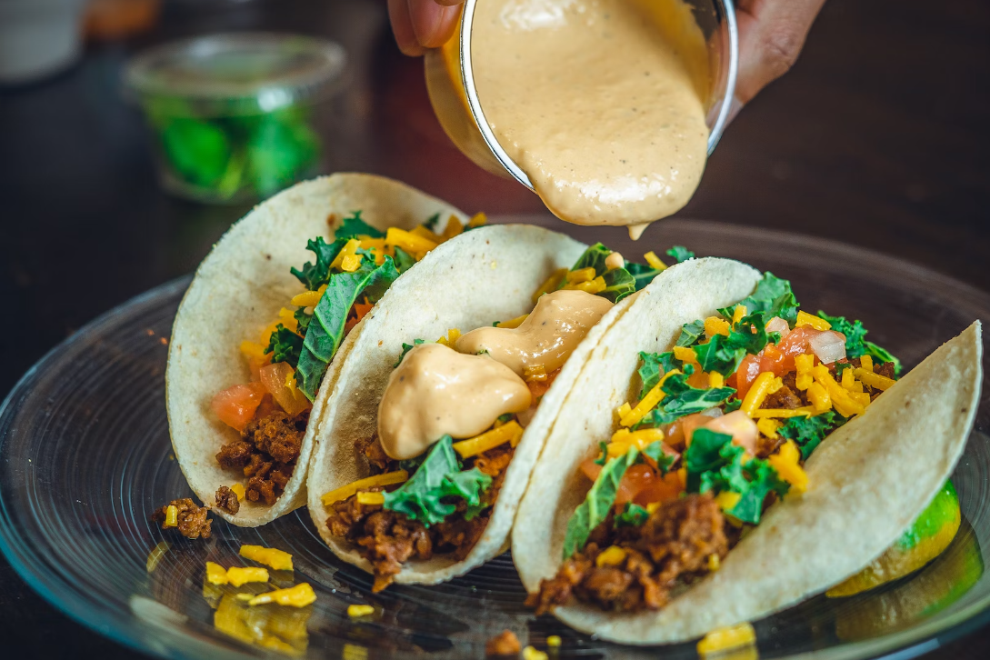 Three tacos on a plate with sauce being poured on top