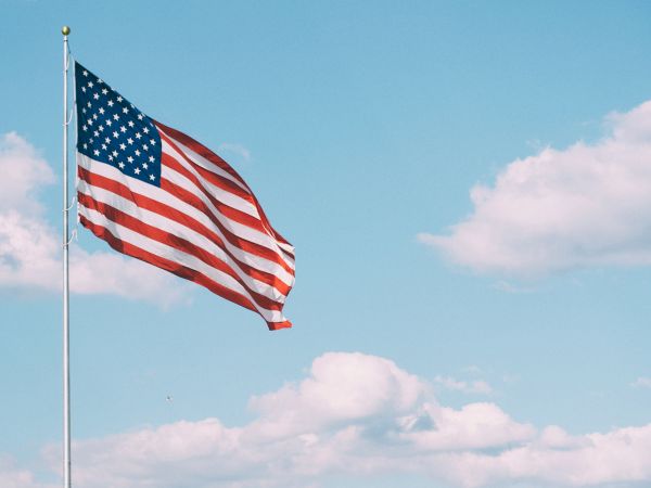 An American flag waves on a pole against a blue sky with scattered clouds, creating a patriotic scene.
