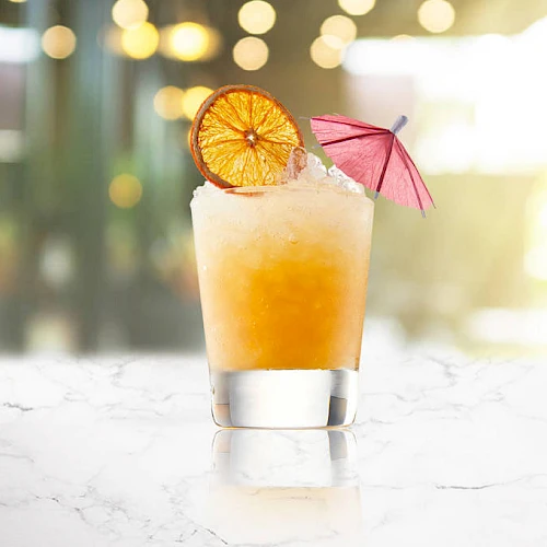 A refreshing cocktail with a gradient orange tint, garnished with a dried citrus wheel and a small pink umbrella on a marble surface.