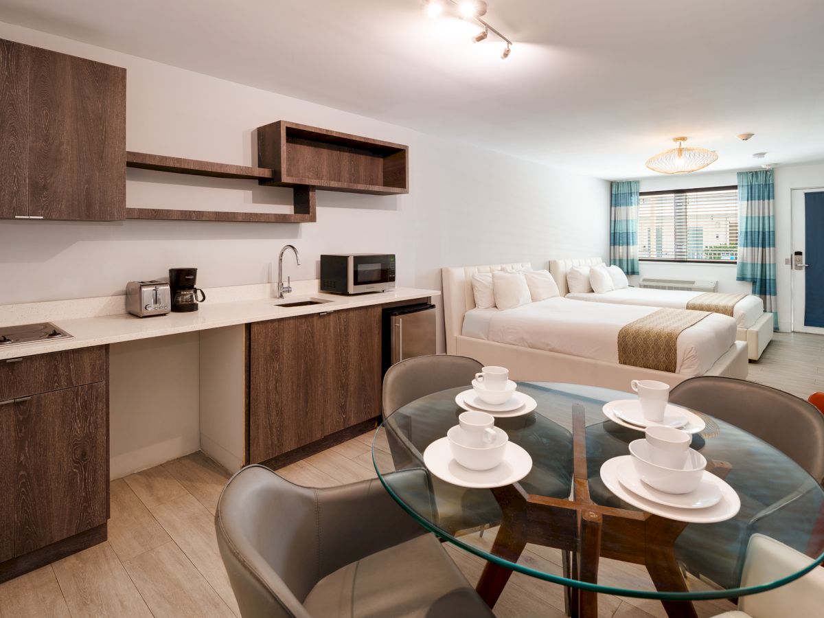 A modern studio with a compact kitchen, dining table set for four, and a cozy living area with a white sofa and blue accents.