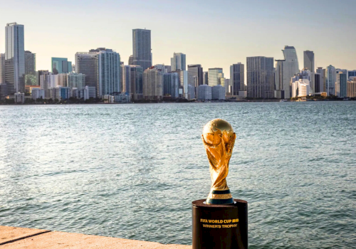 A skyline of tall buildings across a calm bay, with a trophy on a pedestal near the water, reflecting the city&rsquo;s sports victory pride.