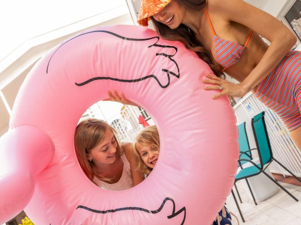 Three kids and an adult by a pool float a pink donut ring, smiling and posing for a fun summer photo.