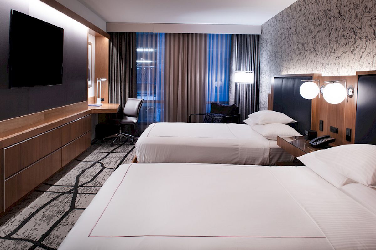 A modern hotel room with two beds, a large TV, desk, and stylish decor.