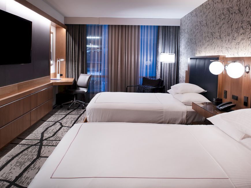 A modern hotel room with two beds, a large TV, desk, and stylish decor.