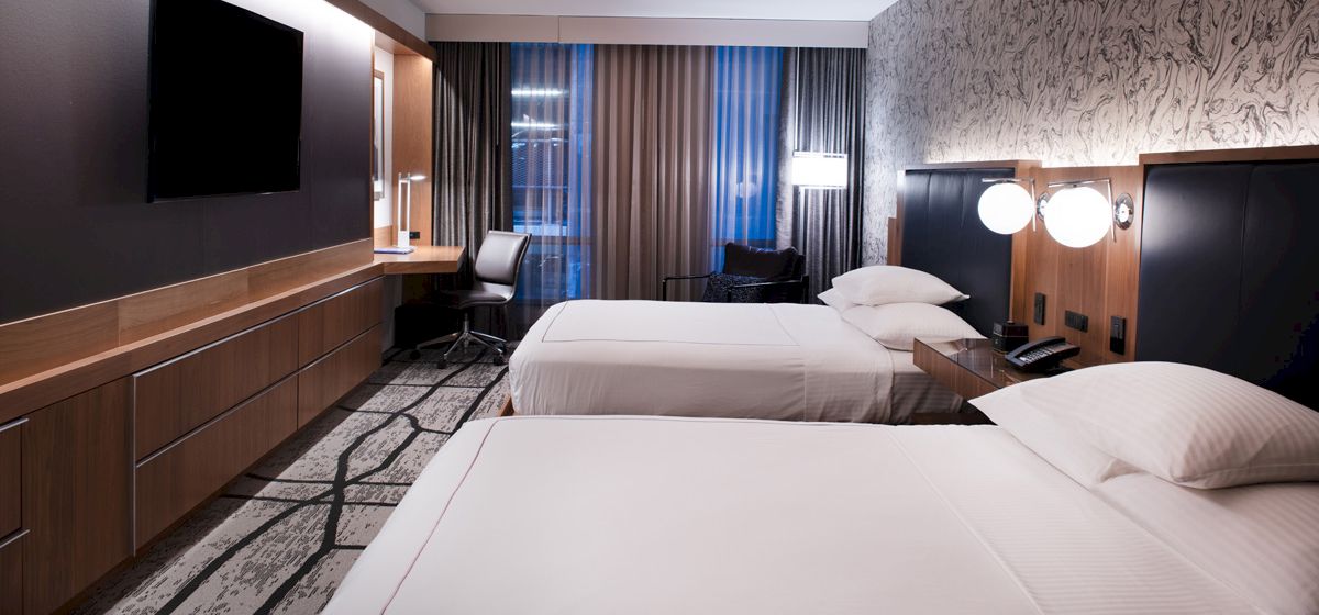 A modern hotel room with two beds, a large TV, desk, and stylish decor.