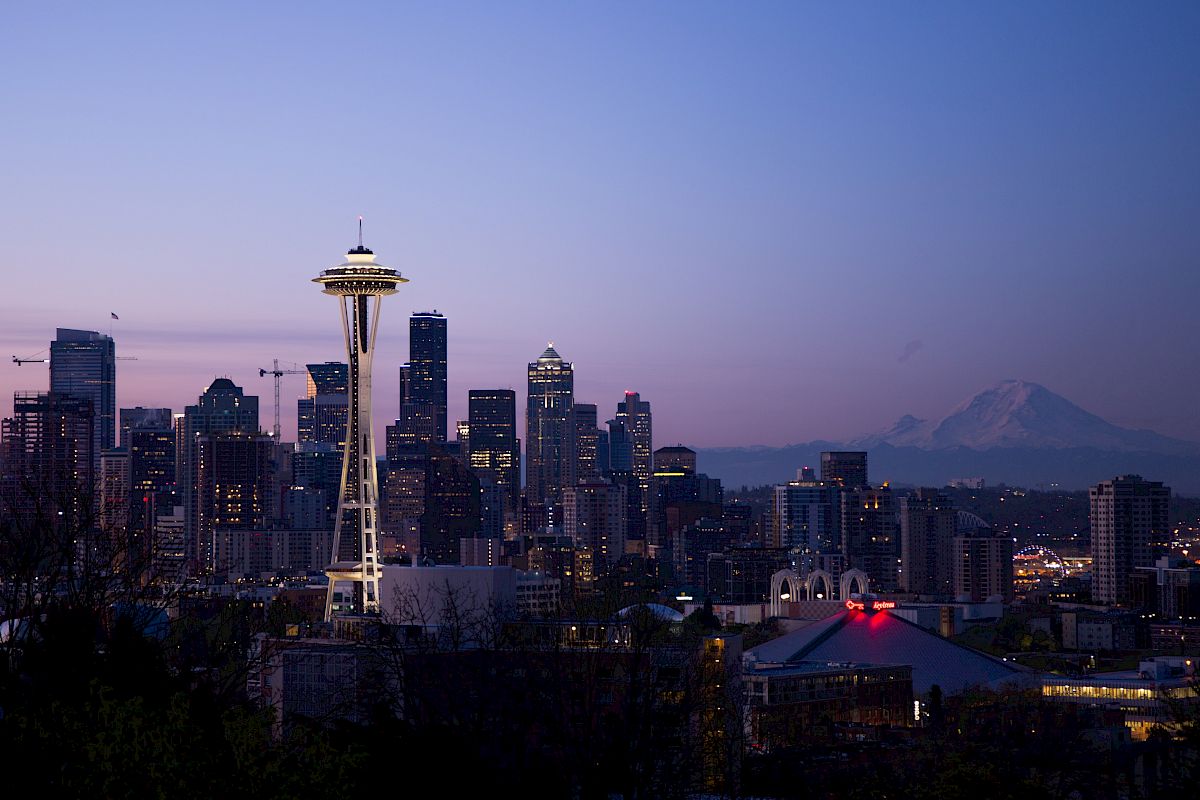 Seattle skyline at dusk with the Space Needle in the foreground and Mount Rainier in the distance under a clear sky.