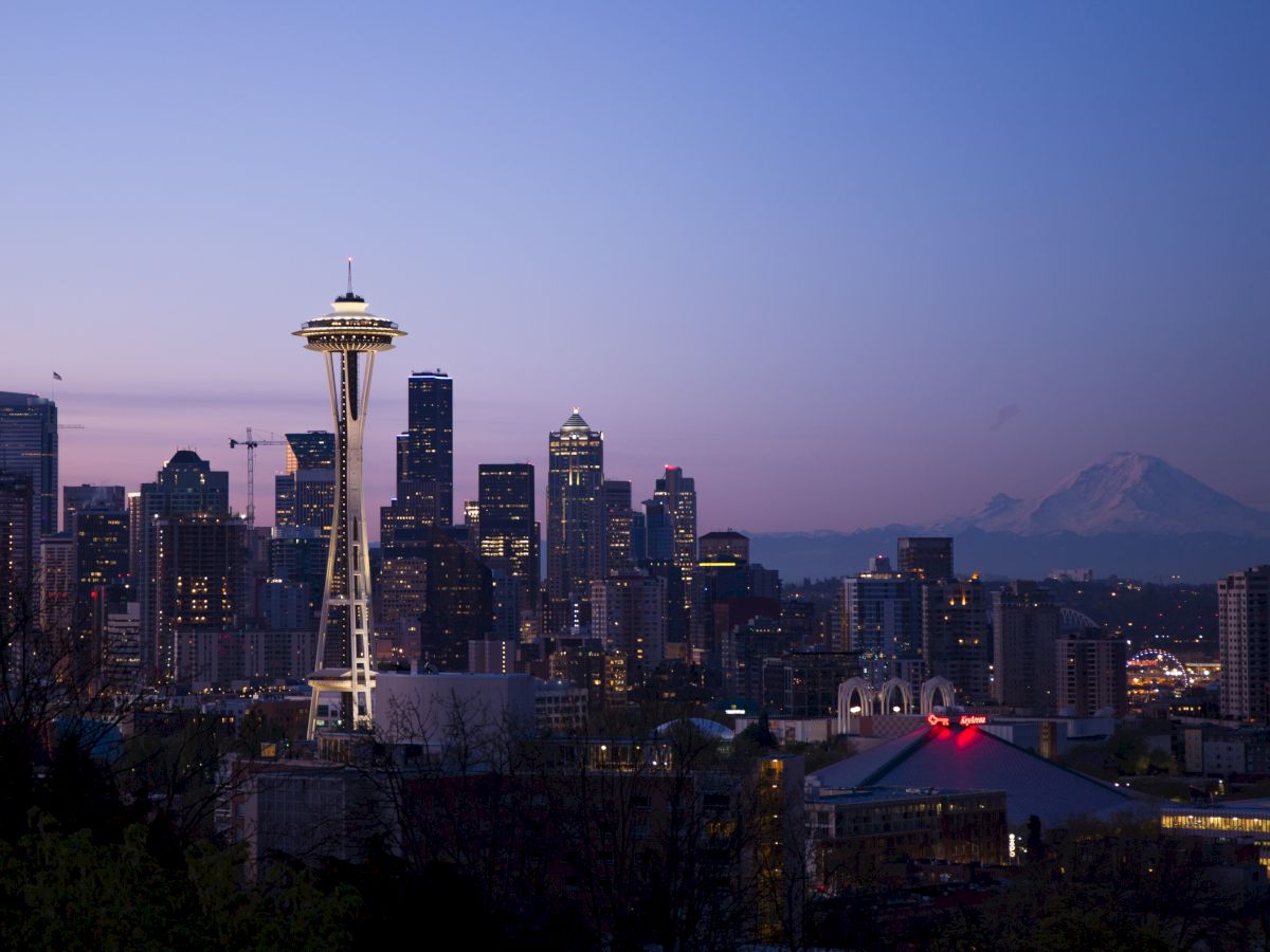 Seattle skyline at dusk with the Space Needle in the foreground and Mount Rainier in the distance under a clear sky.